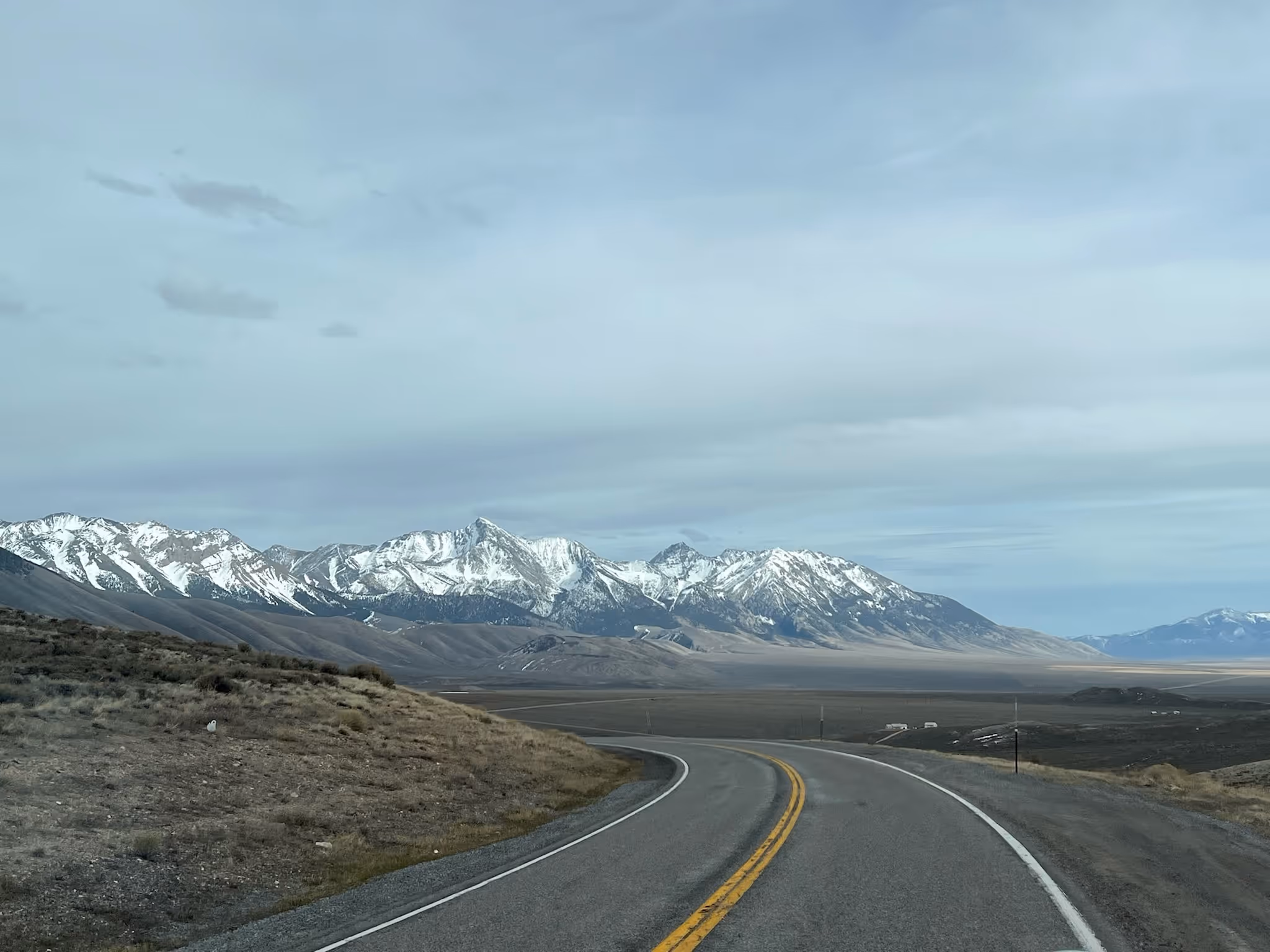 Curving road leading toward distant snow-capped mountains under a cloudy sky.